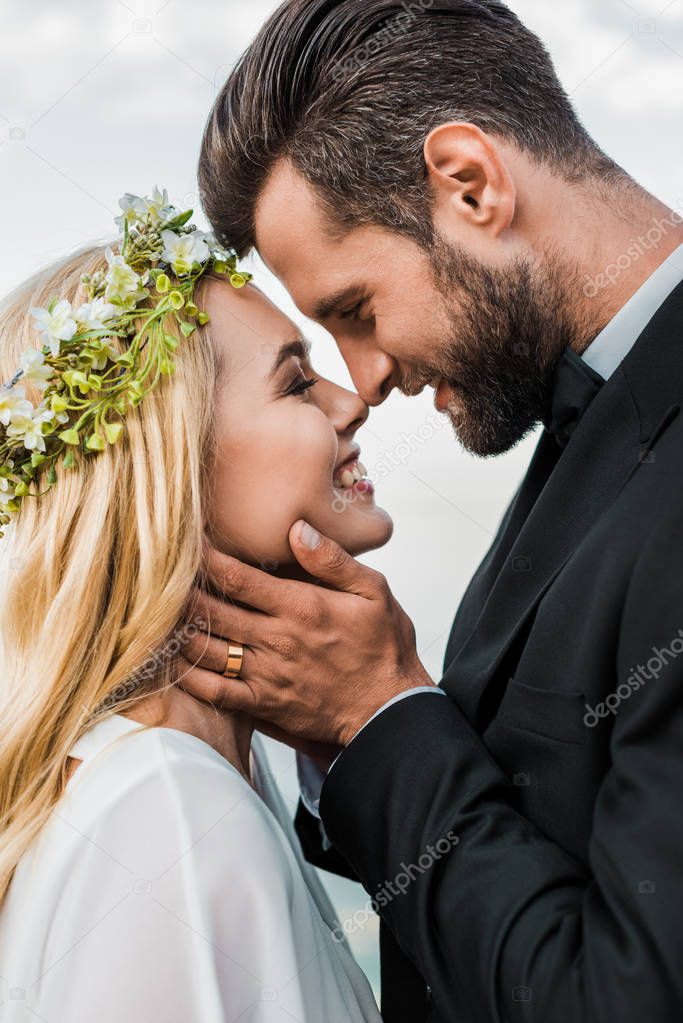 portrait of happy wedding couple in suit and white dress touching with noses on beach