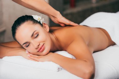young woman with flower in hair having massage therapy at spa salon clipart