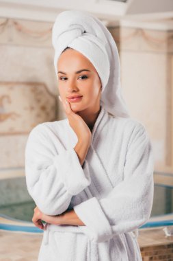smiling woman in white terry bathrobe with towel on head in spa center with swimming pool clipart