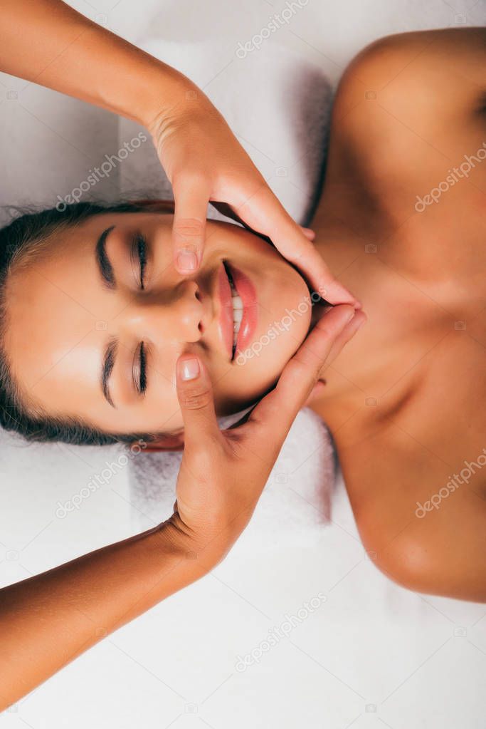 smiling woman relaxing and having face massage in massage salon 