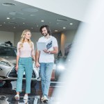 Young couple with catalog buying car at dealership salon