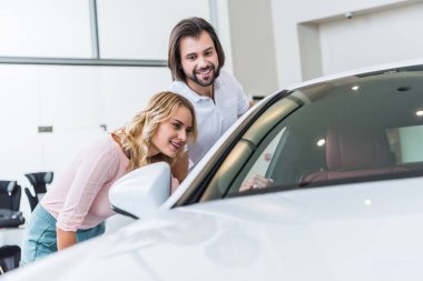 young couple checking new car at dealership salon clipart