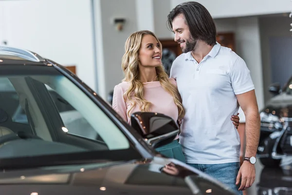 年轻的微笑夫妇选择汽车在经销商沙龙 — 图库照片