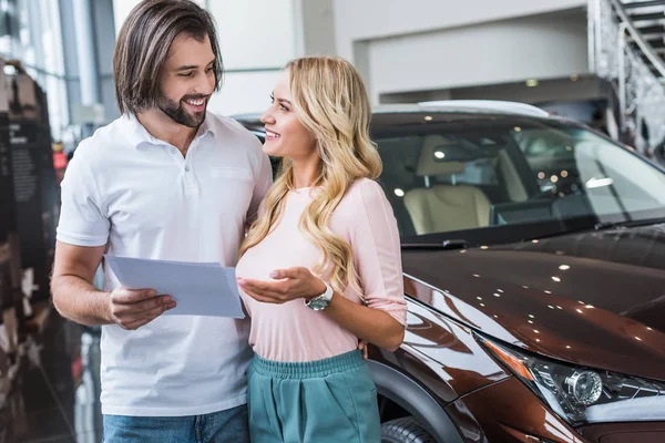 微笑夫妇与目录购买汽车在经销商沙龙的肖像 — 图库照片