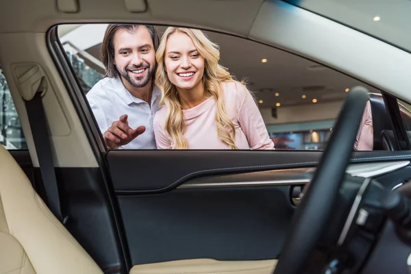 微笑的夫妇在经销商沙龙寻找新的车 — 图库照片