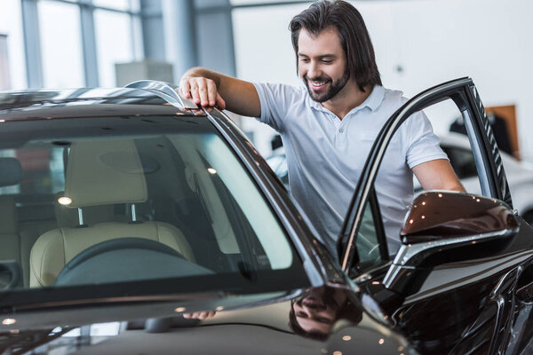 portrait of smiling man standing at new car in dealership salon
