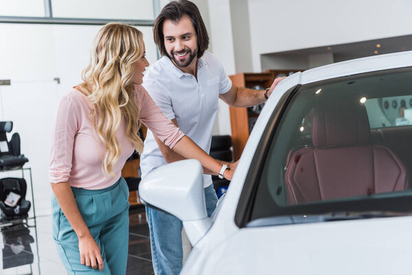 smiling couple choosing car at dealership salon