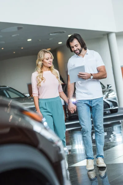 年轻夫妇与目录购买汽车在经销商沙龙 — 图库照片