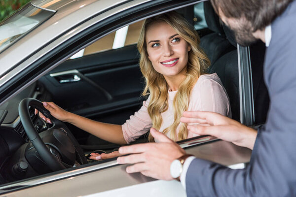 seller in formal wear recommending automobile to woman at dealership salon