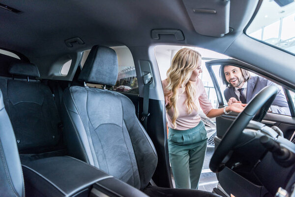 продавец в формальной одежде рекомендует автомобиль женщине в салоне автосалона
