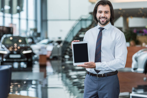 portrait of smiling seller in formal wear showing tablet with blank screen at dealership salon