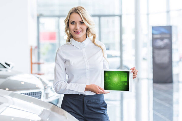 portrait of smiling seller showing tablet with graphic diagram in hands in dealership salon