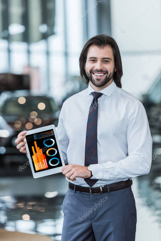 Smiling dealership salon seller in formal wear showing tablet with graphic diagram in hands