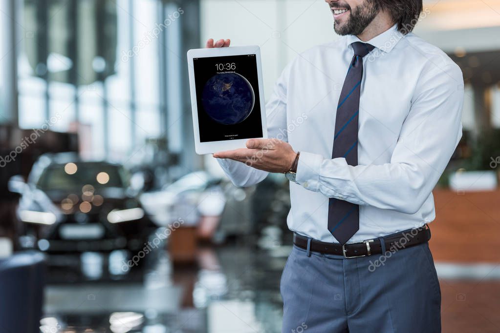 Partial view of dealership salon seller in formal wear showing tablet in hands