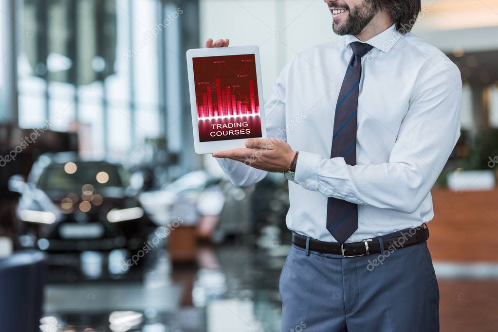 Partial view of dealership salon seller in formal wear showing tablet with trading courses diagram in hands