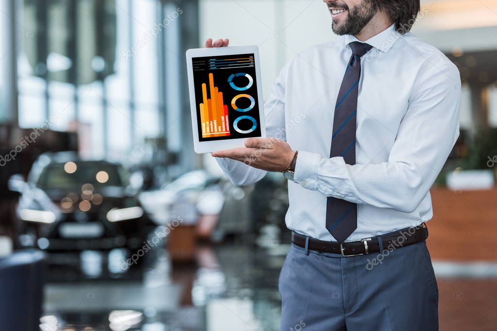Partial view of dealership salon seller in formal wear showing tablet with infographic in hands