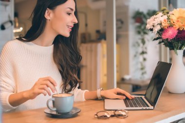 yan görünümü güzel kadın Freelancer laptop masada kafede kahve fincanı ile çalışma 