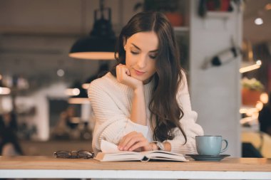 Genç kadın okuma kitabı masada kafede kahve fincanı ile odaklı