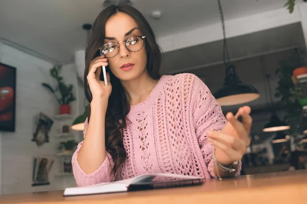 Serious Businesswoman Eyeglasses Woman Talking Smartphone While Writing Textbook Table — Stock Photo, Image