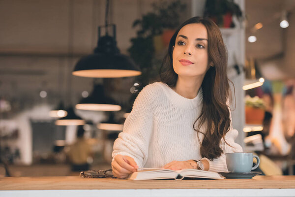 attractive woman reading book at table with coffee cup in cafe