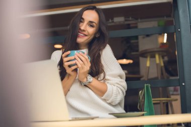 kafede dizüstü bilgisayar ile masada oturmuş kahve fincanı ile neşeli kadın serbest meslek
