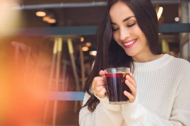 happy young woman holding cup of mulled wine at table in cafe clipart