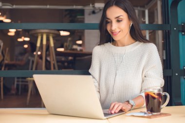 Laptop kafede mulled şarap ile masada çalışma kulaklık içinde kadın serbest meslek gülümseyen