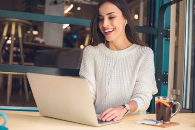 Laptop kafede mulled şarap ile masada çalışma kulaklık kadın serbest meslek gülüyor