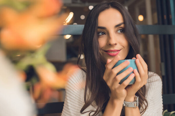 selective focus of pretty woman holding coffee cup at table in cafe 