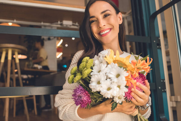 happy young woman holding colorful bouquet from various flowers in cafe