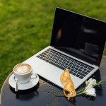 ノート パソコン、コーヒー、サングラス、庭のテーブルの上に花のカップ