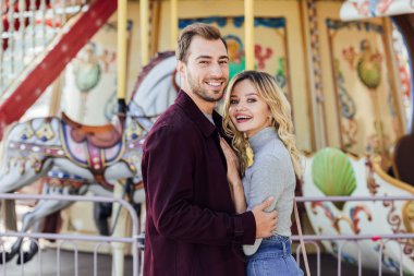 Atlıkarınca amusement park yakınındaki sarılma ve kameraya bakarak sonbahar kıyafeti mutlu sevmek çift