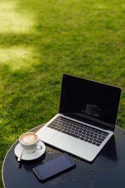 Laptop ve boş ekranlar ve fincan cappuccino'Bahçe tabloda sahip 