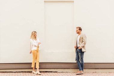 couple in autumn outfit standing near beige wall on street and looking at each other clipart