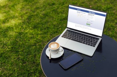 laptop yüklü facebook sayfası, fincan kapuçino ve Bahçe tabloda smartphone ile