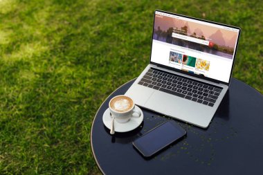 laptop yüklü shutterstock sayfa, fincan kapuçino ve Bahçe tabloda smartphone ile