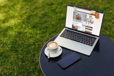 laptop yüklü bbc gıda sayfa, fincan kahve ve smartphone ile Bahçe tabloda boş ekran ile