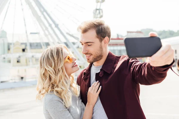 微笑的情侣在秋季服装看着对方 并采取自拍与智能手机在城市 — 图库照片