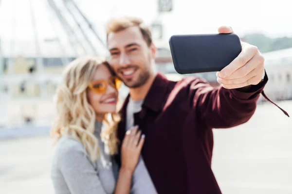 市ではスマート フォンで Selfie を取って秋服のカップルの笑顔の選択と集中  — 無料ストックフォト