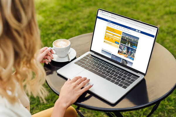 cropped image of woman using laptop with loaded booking page on table in garden