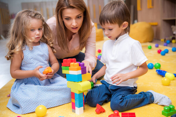 educator and adorable kids playing with constructor in kindergarten