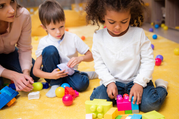 upset african american child playing with colored constructor in kindergarten