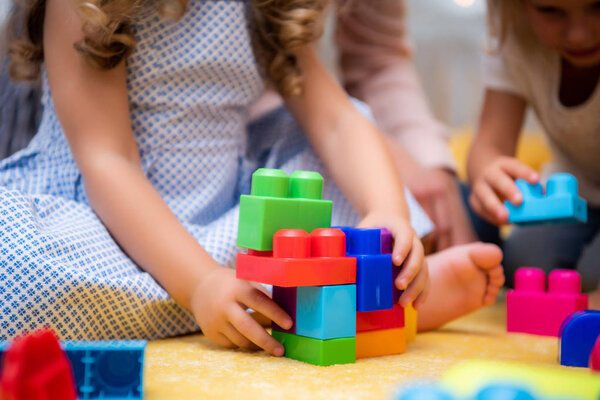 cropped image of kids playing with plastic colored constructor in kindergarten