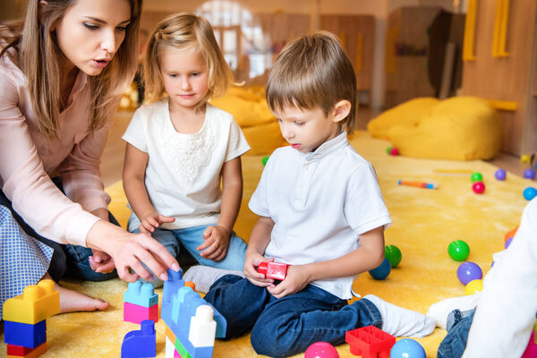 educator and kids playing with constructor in kindergarten