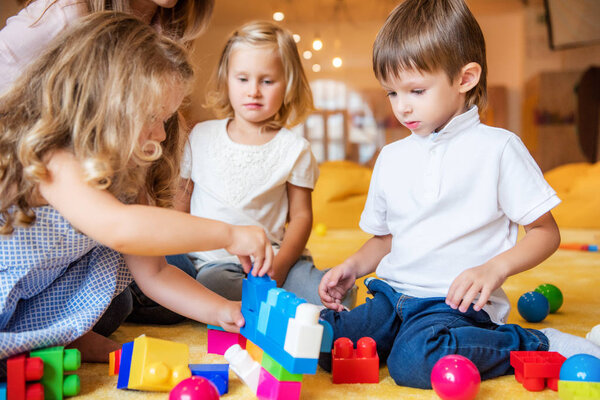 adorable kids playing with constructor on floor in kindergarten