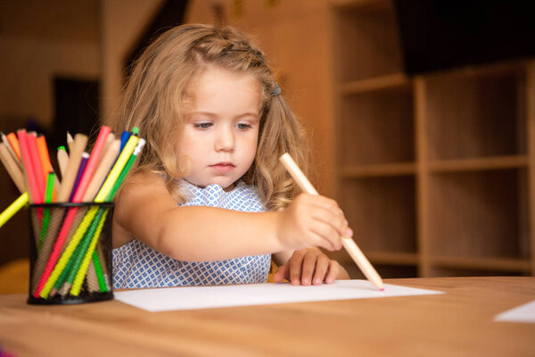 adorable child drawing in kindergarten, pen holder with colored felt tip pens on tabletop