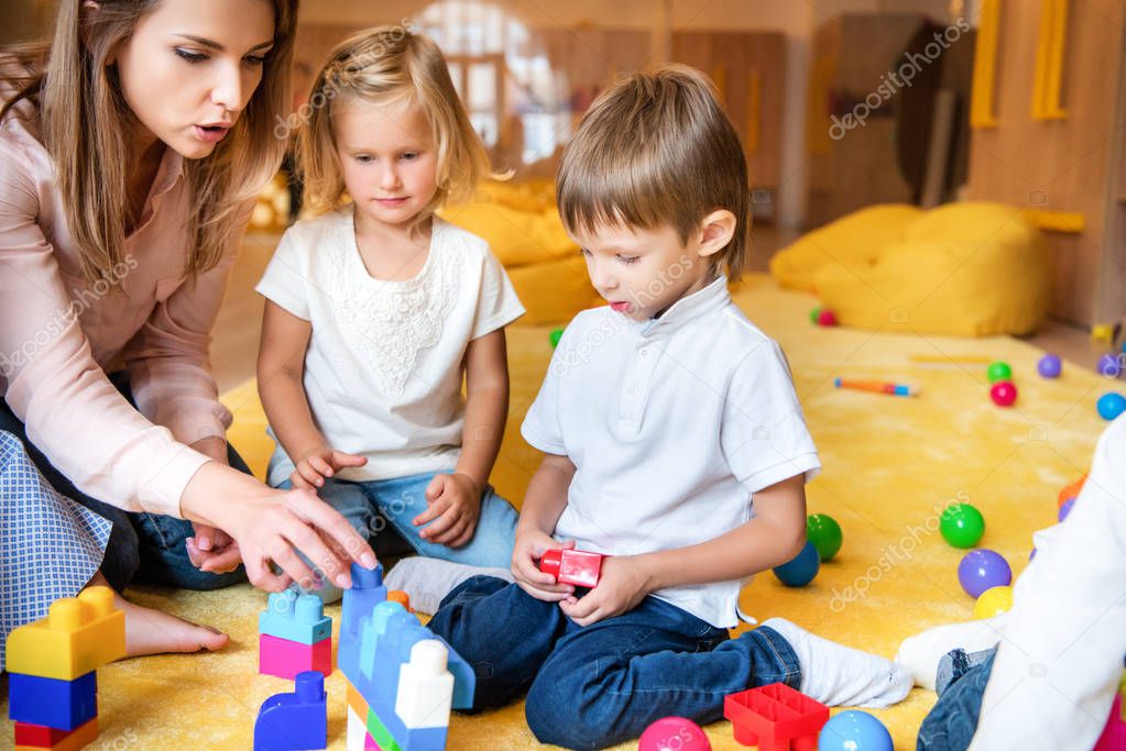 educator and kids playing with constructor in kindergarten