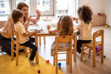eğitimci öğretim sayma ve anaokulunda parmakları ile sayı gösterilen çok kültürlü çocuklar