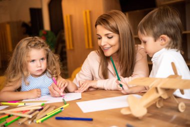 gülümseyen eğitimci anaokulu çocukları ile birlikte çizim