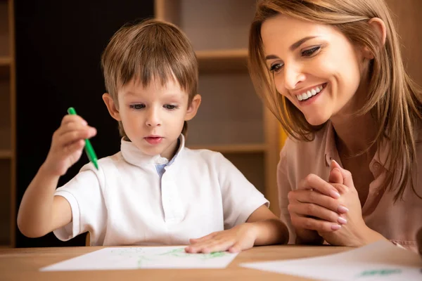 Uśmiechnięty Pedagog Patrząc Rysunek Przedszkolu Chłopiec — Zdjęcie stockowe